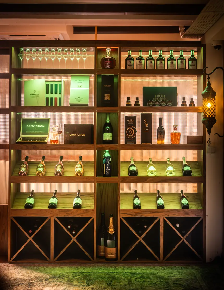 The spirits wall at Casa Marra, lit shelf by shelf, with champagne, single malts and cigar boxes